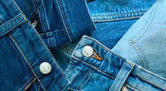 Nahaufnahme von zwei Jeans-Knöpfen und Nähten in verschiedenen Blautönen von Denim, mit einem Reißverschlussansatz und einem kleinen Markenetikett.