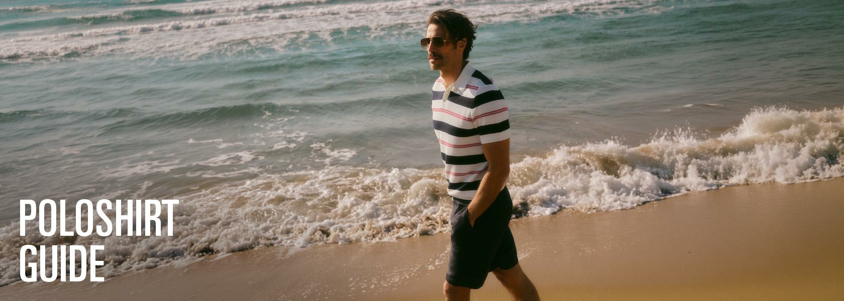 Ein Mann mit Sonnenbrille und gestreiftem Poloshirt geht am Strand entlang. Wellen brechen sich am Ufer.