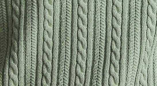 Naheinstellung eines hellgrünen Strickpullovers mit Zopfmuster aus vertikalen Streifen und mehreren geflochtenen Zöpfen