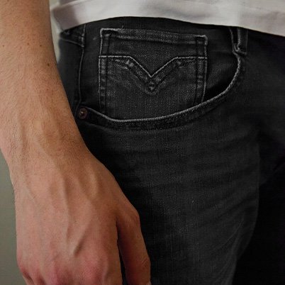 Nahaufnahme einer dunkelgrauen Jeans mit Levi's Logo auf der Gesäßtasche und einer Hand, die leicht auf dem Bein liegt.