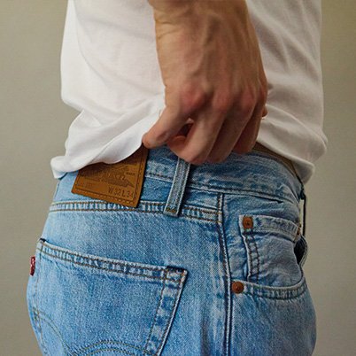 Nahaufnahme eines Mannes mit heller Jeans und weißem T-Shirt, der an das Etikett greift.