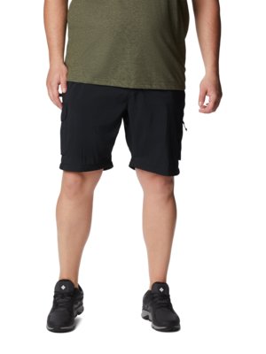 Mann trägt schwarze Cargo-Shorts und ein olivgrünes T-Shirt. Er trägt schwarze Sportschuhe. Ganzkörperaufnahme vor weißem Hintergrund.