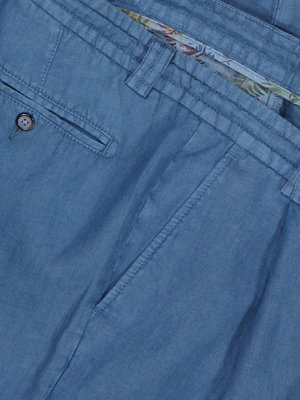 Nahaufnahme von blauem Leinenstoff, gefaltet und übereinandergelegt.  Man sieht Details wie Naht, Knöpfe und einen Teil eines blumigen Innenfutters.