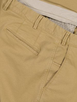 Close-up of tan cotton pants; showing waistband, pockets, and stitching detail. The fabric appears lightweight. The pants are folded, showcasing the interior waistband.