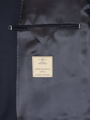 Close-up of dark grey suit jacket interior lining showing a woven texture. A small beige label reads "Officina Waldaigno," "SUPER 120's WOOL," "Stretch," and "Exclusively for DIESEL." Metal loops are visible at the top corners of the lining.
