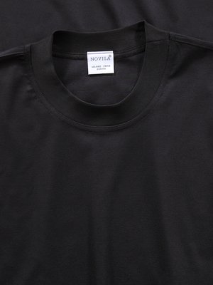 Nahaufnahme eines schwarzen T-Shirts mit Rundhalsausschnitt. Ein kleines Etikett mit dem Schriftzug „NOVILA“ ist sichtbar. Das Shirt wirkt aus Baumwolle oder einem ähnlichen Stoff gefertigt.