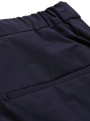 Close-up of dark blue fabric, showing a waistband with gathered elastic. Below the waistband is a patch pocket. The fabric is slightly wrinkled.