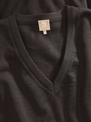 Nahaufnahme eines dunklen V-Ausschnitt-Pullovers. Ein Etikett mit der Aufschrift "M Mario" ist am Ausschnitt befestigt. Die Strickstruktur des Stoffes ist erkennbar.