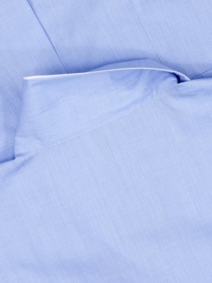 Nahaufnahme eines hellblauen Hemdkragens mit weißem Saum. Der Stoff hat eine feine Struktur, die Falten und eine Naht in der Mitte zeigen. Der Kragen ist leicht gebogen.