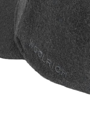 Nahaufnahme einer dunklen Mütze aus Wollstoff. Der Schriftzug "WOOLRICH" ist dezent auf der Oberfläche der Mütze zu erkennen. Die Mütze ist leicht gewölbt.