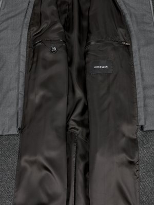 Close-up view of the inside of a gray suit jacket showing smooth black lining, one buttoned pocket, and a zippered pocket.