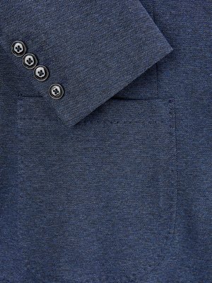 Detailaufnahme eines dunkelblauen Blazer-Ärmels. Der Ärmelstoff ist aus grob gewebtem Material. Auf dem Ärmel befinden sich vier schwarze Knöpfe mit weißem Innenteil. Der Fokus liegt auf dem Ärmel und dem Saum der Brusttasche.