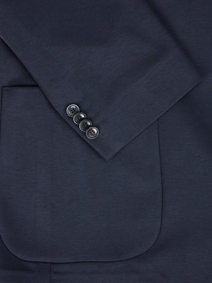 Nahaufnahme eines dunkelblauen Blazer mit einem abgerundeten Taschensaum und Ärmel mit vier Knöpfen. Die Knöpfe sind dunkelgrau mit roten Fäden.