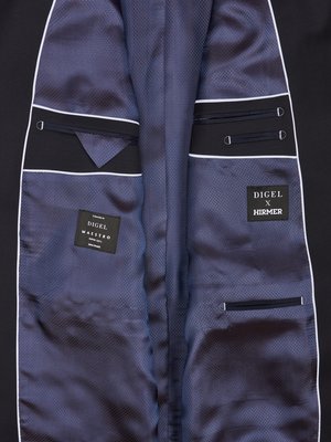 Nahaufnahme des Innenfutters eines schwarzen Sakkos. Blaues Futter mit kleiner Musterung. Auf der linken Seite befinden sich zwei Taschen, rechts ebenfalls, mit Details. Auf der rechten Seite steht "DIGEL X HIRMER", links "DIGEL MAESTRO".