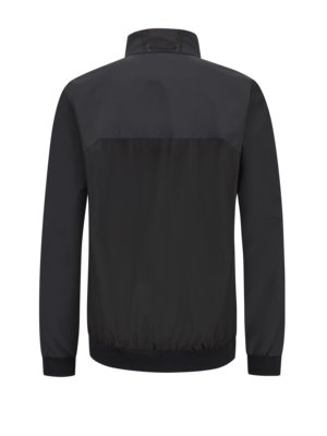 Back view of a black jacket with a high collar. The jacket has long sleeves, a black waistband, and a contrasting panel across the shoulders. A small loop is at the back of the collar.