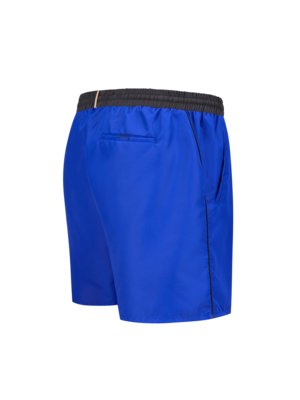 Eine blaue Badeshorts, die von hinten und von der Seite gezeigt wird. Die Badeshorts hat einen schwarzen Gummibund, eine Tasche und eine dünne, schwarze Naht an der Seite. Der Hintergrund ist weiß.