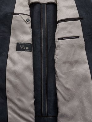Innenansicht eines dunkelblauen Sakkos. Auf der Innenseite ist hellgraues Futter mit einem dezenten Muster zu sehen. Schwarze Paspeltaschen und ein Label sind sichtbar. Die Nähte sind hell.