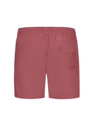 Back view of a pair of short swim trunks in a muted red color. The shorts have an elastic waistband and a single patch pocket on the right side. A small logo is visible on the pocket.