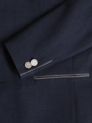 Close-up of a navy blue blazer sleeve with two silver buttons at the cuff. A pocket with a gray trim is visible. The blazer appears to be made of a textured fabric.