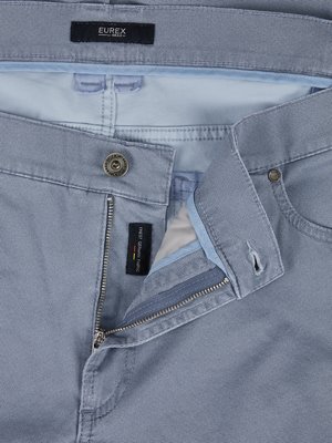 Nahaufnahme einer hellblauen Jeanshose. Der Reißverschluss ist geöffnet. Über der Knopfleiste ist ein Knopf, darüber ein schwarzes Etikett mit dem Wort "EUREX". Ein weiteres Etikett ist an der Innenseite zu sehen.