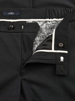 Nahaufnahme einer geöffneten dunklen Hose. Der Reißverschluss ist halb geöffnet, der Bund ist mit Knöpfen und Haken verschlossen. Innenfutter mit floralem Muster und weißer Paspelierung. Auf der Hose ein "Eurex" Label.
