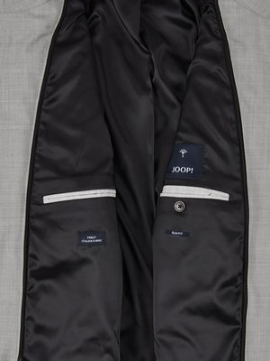 Nahaufnahme des Innenfutters eines hellgrauen Sakkos. Innenfutter schwarz. Aufgenähte Taschen mit weißen Paspeln. Links "FINEST ITALIAN FABRIC" und rechts ein Knopf sowie ein Joop!-Label.