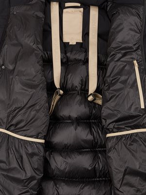 Close-up interior view of a black puffer jacket. Visible are padded sections, beige straps with "WOOLRICH" printed on them, a small beige label, and a beige zipper detail.