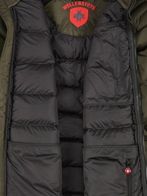 Nahaufnahme des Innenfutters einer olivgrünen Jacke. Die Jacke hat einen schwarzen Steppbereich mit sichtbaren Nähten, seitlich zwei Taschen. Oben mittig ein rotes Logo. Ein Reißverschluss an der rechten Tasche.