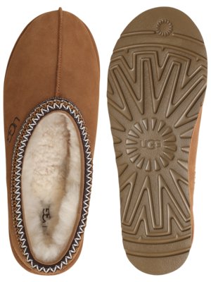 Two brown UGG slippers are displayed. One slipper is upright, showing the top with decorative stitching around the opening and the UGG logo. The other is flipped to show the brown sole with the UGG logo and textured tread.