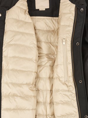 Nahaufnahme einer schwarzen Jacke, geöffnet, mit cremefarbenem, gesteppten Innenfutter. Der Reißverschluss, die Knöpfe und ein Etikett im Kragen sind ebenfalls sichtbar.