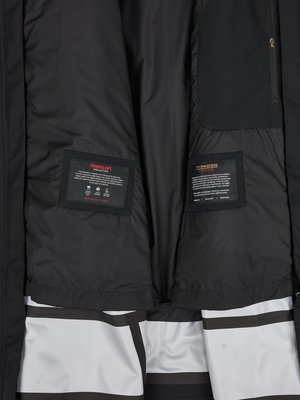 Die Innenseite einer schwarzen Jacke, mit zwei rechteckigen Etiketten, die "PRIMALOFT" und "TYPHOON" beschriften. Die Jacke hat außerdem eine Innentasche und eine helle, gestreifte Unterseite. Der Stoff ist schwarz.