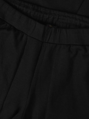 Close-up of black fabric. The image focuses on the waistline of what appears to be pants. The waistline has a gathered, textured area. Vertical seams run down the front of the pants.