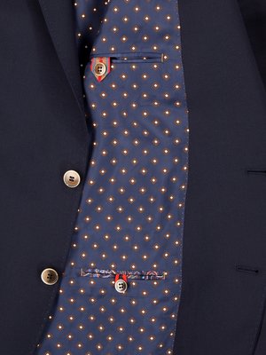 Nahaufnahme einer dunkelblauen Jacke, geöffnet, um das Innenfutter zu zeigen. Innenfutter ist blau mit weißen Rauten und kleinen gelben Punkten. Zwei Knöpfe sind sichtbar, sowie eine Brusttasche.