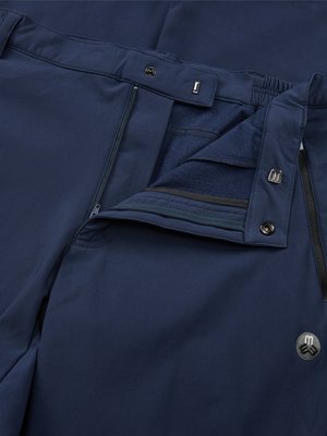 Close-up of open navy blue pants. A zipper is partially unzipped. The pants have a button closure at the waistband and a branded metal button near the pocket.