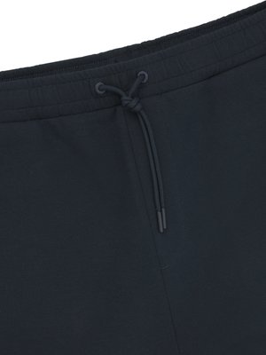 Close-up of dark blue fabric, possibly athletic pants. A drawstring with a knot and two dangling cords is centered at the top. The fabric is smooth and appears to be slightly textured.