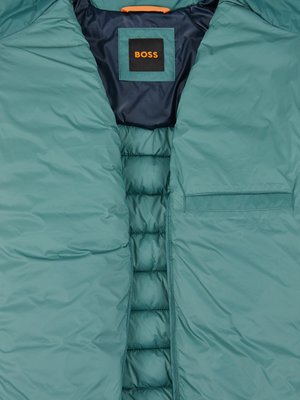Nahaufnahme einer wattierten Jacke in Türkis mit einem sichtbaren BOSS-Logo-Etikett innen.