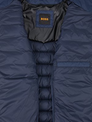 Nahaufnahme einer blauen Daunenjacke. Ein schwarzer Kragen und ein Etikett mit der Aufschrift "BOSS" sind zu sehen. Die Jacke hat einen Reißverschluss und eine kleine Tasche. Das Steppmuster ist deutlich sichtbar.