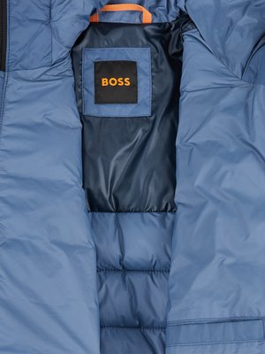 Close-up interior view of a blue puffer jacket. The jacket has a dark blue lining with a BOSS brand tag. The hood lining and details are orange. The image emphasizes the jacket's texture.
