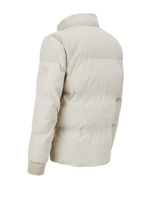Rückansicht einer hellbeige Steppjacke. Die Jacke hat einen Stehkragen, lange Ärmel mit gerippten Bündchen und einen kleinen Logoaufnäher am linken Ärmel. Die Jacke hat horizontale Steppnähte.