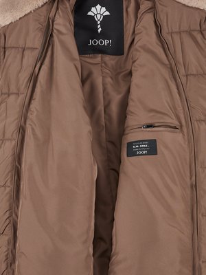 Innenansicht einer braunen Jacke. Innenfutter mit zwei Taschen. Oben mittig ein schwarzes Etikett mit JOOP! Logo. Am Kragen Fellbesatz. Auf einem weiteren Etikett steht JOOP! und weitere Informationen.