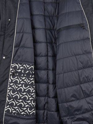 Detailansicht der Innenseite einer dunkelblauen Jacke. Auf der rechten Seite eine gesteppte, glatte Oberfläche. Links ein Innenfutter mit weißem Muster auf dunklem Hintergrund. Oben eine kleine Reißverschlusstasche.
