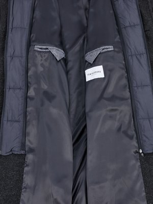 An open grey winter coat with a dark gray interior is shown from the inside. Padded panels border the interior. Inside are two grey pockets, and a white label that reads TOM RUSSBORG.