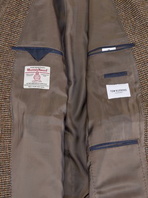Vnitřek hnědého pánského saka s tvídovým vzorem. Viditelné kapsy s modrými lemy a dvě cedulky: Harris Tweed a Tom Rusborg. Zdobené podšívkou a s logem.