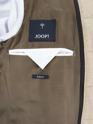 Blick auf das Innenfutter einer beigen Jacke mit schwarzem JOOP! Logo und Slim Fit Etikett, sowie einer weißen Tasche.