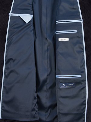 Nahaufnahme des Innenfutters eines dunklen Cord-Sakkos. Die Innenseite ist dunkelblau mit verschiedenen Taschen und Nähten. Ein hellblaues Dreieck, ein Etikett "Regular Fit" und ein weiteres mit Text "Bottom" sind zu sehen.