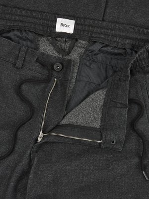 Close-up view of dark gray trousers, partially unbuttoned. Visible details include a black drawstring, a silver zipper, and a button. The brand label "Brax" is visible. The inside lining is light gray.