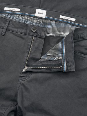 Nahaufnahme einer grauen Hose mit Reißverschluss, offenem Knopf und sichtbarer Innenfutter-Stoff. Auf dem Hosenbund sind die Markenbezeichnungen "Marathon", "Brax" und "Style Cella" zu erkennen.