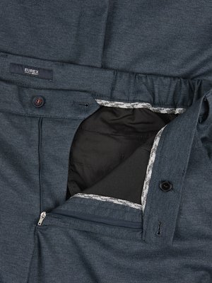 Nahaufnahme einer geöffneten blauen Hose. Der Reißverschluss und ein Knopf sind geöffnet. Innen ist der dunkle Stoff des Hosenfutters sichtbar. Ein Markenetikett mit "EUREX" ist zu sehen. Der Bund hat ein graues Muster.