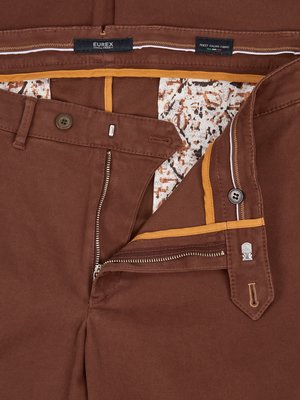 Nahaufnahme einer geöffneten braunen Hose mit Reißverschluss, Knopf und Knopfleiste. Der Bund hat ein Innenfutter mit weißem und braunem Muster. Auf dem Bund ist ein Etikett "EUREX" zu sehen.