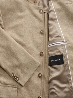 Nahaufnahme einer beigefarbenen Herrenjacke. Die Jacke ist aus Stoff gefertigt und hat eine Reihe von Knöpfen sowie eine Innentasche mit dem Markennamen Dressler. Der Ärmel liegt links.
